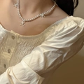 Collier de perles élégant avec pendentifs nœuds argentés porté sur un chemisier à volants - Collier de Perles avec Nœud