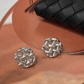 Dettaglio di orecchini intrecciati geometrici in argento su pelle marrone - Argento