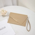 Light brown envelope clutch with gold metal bar trim and wrist strap on a white table - Khaki