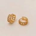 Dettaglio macro di orecchini a cerchio dorati con zirconi micro-pave e intagli geometrici - Oro