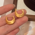 Detalle de pendientes en forma de U de oro mate con textura cepillada en los dedos - Oro Cepillado