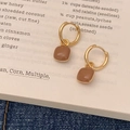 Minimalistische bruine hars oorbellen met gouden ringen op een boekenachtergrond - Melkthee Kleur