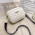 Détail du sac bandoulière crème matelassé avec large sangle tissée sur parquet clair - Blanc
