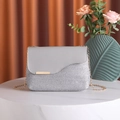 Bolso tejido plateado con solapa gris y cadena dorada sobre mesa de mármol - Gris