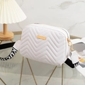 White V-quilted camera bag with wide woven strap and gold metal trim on glass surface - White