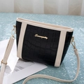 Detail of black crocodile texture bucket bag with white trim and gold logo on teal surface - Beige and Black