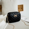 Black quilted crossbody bag with gold bow detail and chain strap in a cozy home setting - Black (Bow)