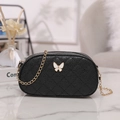 Quilted black crossbody bag with butterfly buckle and gold chain strap in a lifestyle setting - Black