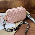 Pink quilted crossbody bag with wide logo strap displayed on a brown leather sofa - Pink
