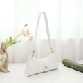 White underarm bag with embossed texture and golden circular clasp on white desk - White