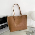 Braune Shopper-Tasche mit Faltentextur und Quastenanhänger auf einem Schreibtisch - Gelbbraun
