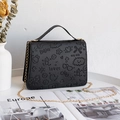 Black embossed handbag with playful patterns and gold chain strap on a white desk - Black