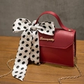 Red mini handbag with large polka dot bow and gold chain on a wooden table - Red