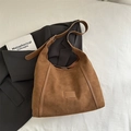 Braune Wildleder-Schultertasche mit Glattlederbesatz auf schwarzem Blazer-Hintergrund - Braun