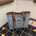 Light blue denim tote bag with brown leather trim and fashion label on checkered surface - Blue