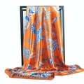 Golden phoenix paisley silk scarf in orange and blue displayed on a sleek black metal rack - Orange
