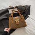 Women's brown monogram tote bag with gold M-buckle on a black blazer background - Brown