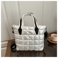 Detail of pearl white quilted tote bag with black handles on a wooden table - White