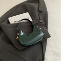 Bolso medialuna verde oscuro en charol con herrajes dorados sobre chaqueta gris - Verde