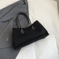 Detail of minimalist black matte tote bag resting on a professional grey blazer suit - Black