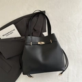 Minimalist black leather bucket bag with gold turn-lock and drawstring closure detail - Black
