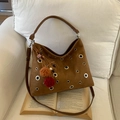 Bolso tote de ante marrón con ojales metálicos y pompón de cuadros sobre un libro - Sin Colgante / Marrón