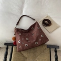 Close-up of coffee brown suede crossbody bag with silver eyelets and a red pompom charm - Coffee (With Pendant)