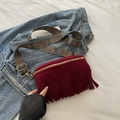 Burgundy suede tassel waist bag with a vintage bohemian patterned strap shown on denim - Red