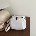 Trendy white canvas crossbody bag with black dual zippers on a wooden table setup - White