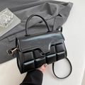 Structured black handbag with geometric pattern and top handle in a lifestyle setting - Black