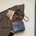 Bolso de tela vaquera con ribete de cuero marrón y correa ajustable sobre una chaqueta - Azul