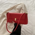 Red leather baguette shoulder bag with gold metal clasp shown with a beige blazer - Red