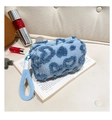 Detail of light blue sherpa makeup bag with navy hearts and rope handle on vintage book - Blue