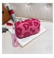 Detailed close-up of a plush magenta heart cosmetic bag on an open book in soft lighting - Rose Red