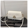 Detailed close-up of cream leather crossbody bag with golden arch buckle on black books - White