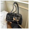 Close-up of black glossy shoulder bag featuring dual pockets with bow details and silver studs - Black