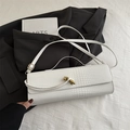 Sac à main blanc effet crocodile avec fermoir doré posé sur une veste de costume noire - Blanc