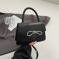 Black crocodile pattern handbag with rhinestone bow on gray suit jacket background - Black