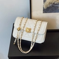 Elegante borsa bianca a tracolla trapuntata con catena dorata su un tavolo nero lucido - Bianco Sporco