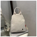 Dettaglio dello zaino in nylon beige con etichetta rossa e logo metallico circolare - Beige