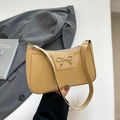 Sac porté épaule beige avec boucle nœud dorée, présenté devant un costume gris - Kaki