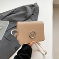 Minimalist beige woven square crossbody bag with metallic M logo on a grey suit background - White