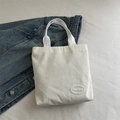 White corduroy tote bag with thick ribbon handles and logo patch on denim backdrop - White