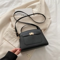 Sac à main noir en cuir grainé avec fermoir doré posé sur une veste chic blanche - Noir