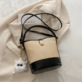 Beige and black bucket bag with gold clasp and plush charm in lifestyle setting - With Pendant / Black