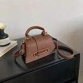 Détail d'un sac bandoulière en cuir grainé marron avec finitions dorées et poignée - Marron