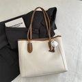 Detail of a minimalist tote bag in beige faux leather with brown trim and plush charm - White With Pendant