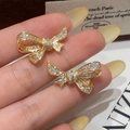 Detalle de pendientes de lazo dorado con circonitas pavimentadas sobre fondo de revista - Pendientes de Botón de Lazo / Dorado