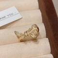 Detalle de un anillo de lazo dorado con circonitas en un joyero de terciopelo beige - Anillo de Lazo / Dorado