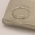 Detail of adjustable silver metal bracelet with curved bar and twist knot on ceramic tray - Silver
